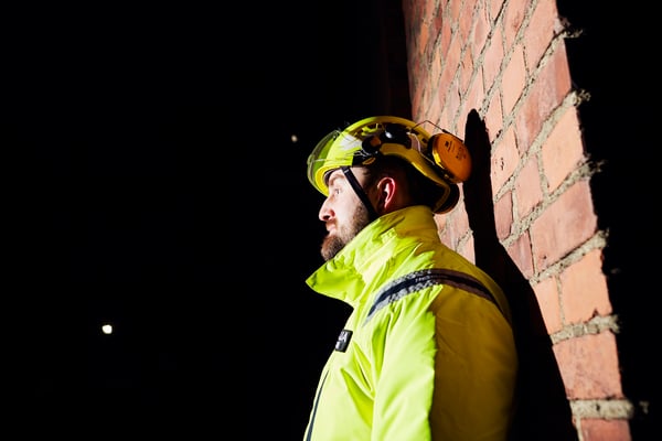 ISS:n vartija heijastintakissa, päässään kypärä ja suojalasit, pimeällä tehdasalueella.