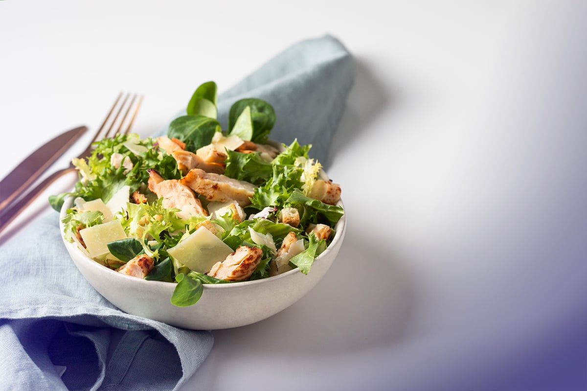 Annos Caesar-salaattia valkoisessa kulhossa lautasliinan päällä, valkoisella taustalla.