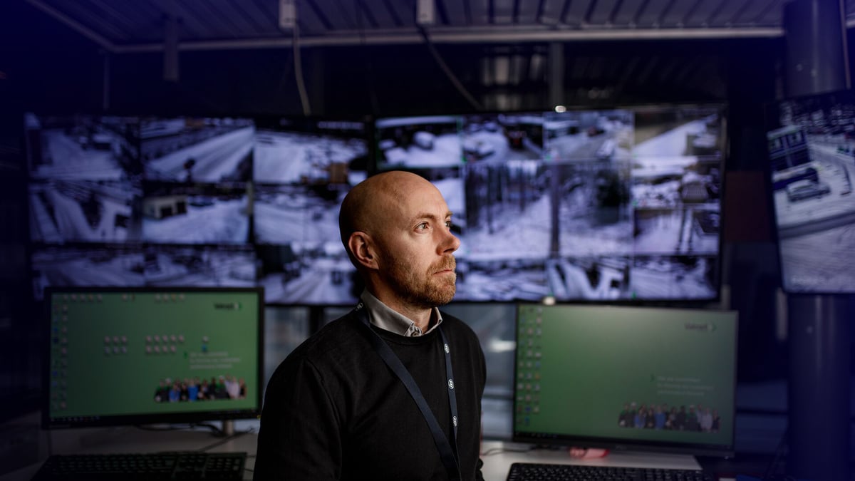 ISS:n työntekijä valvomossa, takanaan valvontakameran kuvaa koko taustan peittävillä näytöillä.