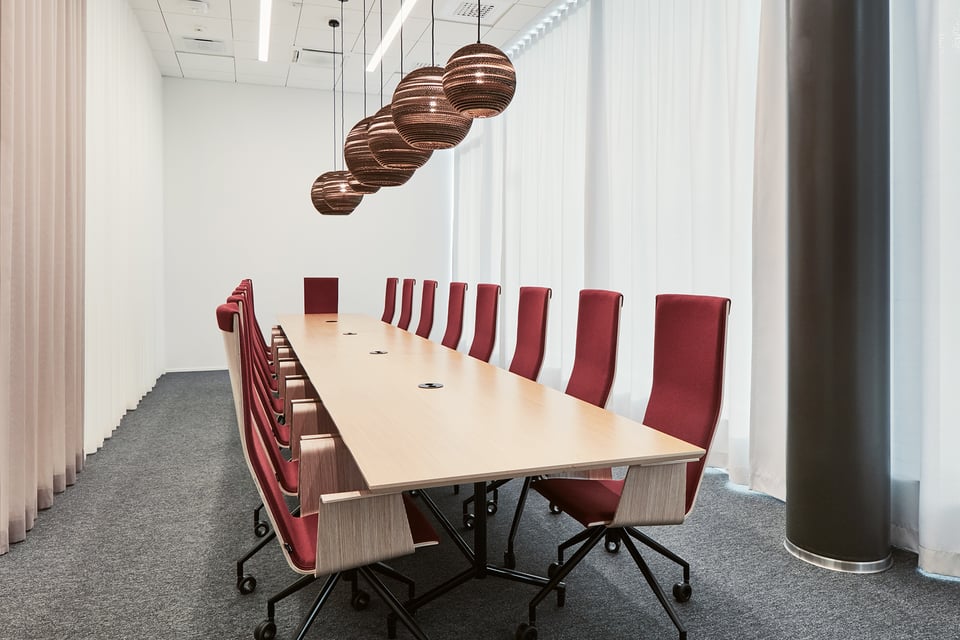 Ultimes Business Gardenin Loiste-kokoustila, jossa pitkän puisen pöydän äärellä 17 punaista työtuolia, ja pöydän yläpuolella pyöreitä kattovalaisimia.