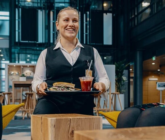 ISS:n kahvilatyöntekijä polvistunut tarjoilemaan voileivän ja smoothien tarjottimella toimistorakennuksen aulakahvilassa.