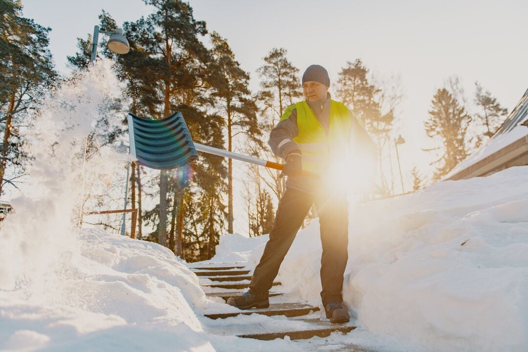 Kiinteistöhuoltaja lapioi lunta.