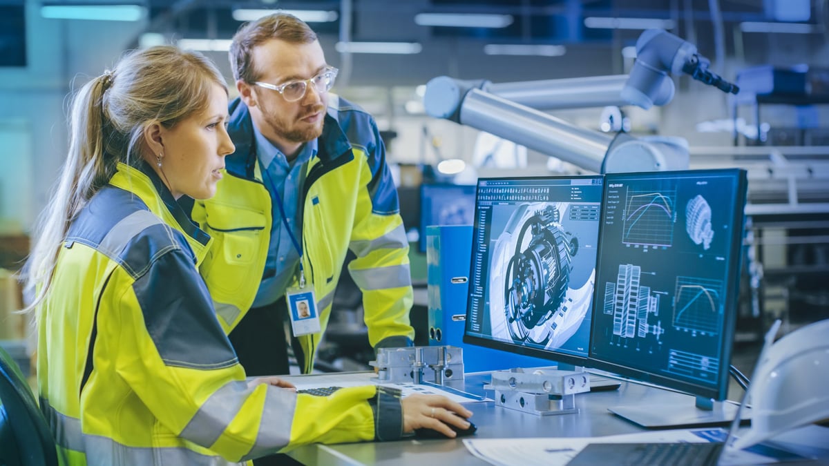Nainen ja mies tietokoneen äärellä tutkimassa teollisen komponentin piirrustuksia yllään heijastintakit.